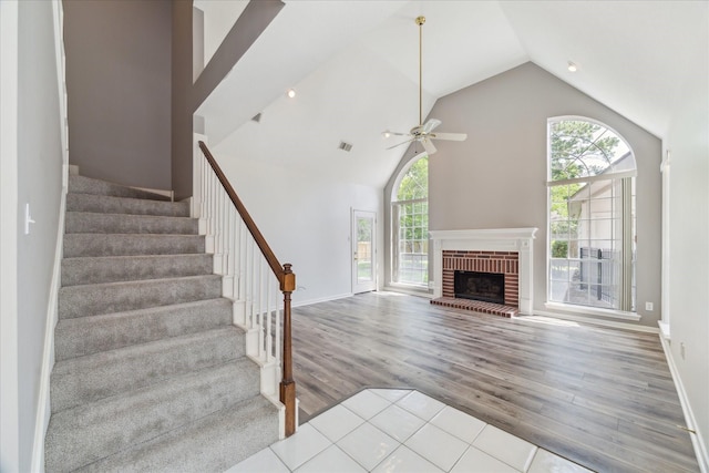 unfurnished living room featuring wood finished floors, a ceiling fan, stairway, a fireplace, and high vaulted ceiling