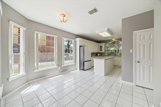kitchen with freestanding refrigerator, light tile patterned flooring, baseboards, a center island, and glass insert cabinets