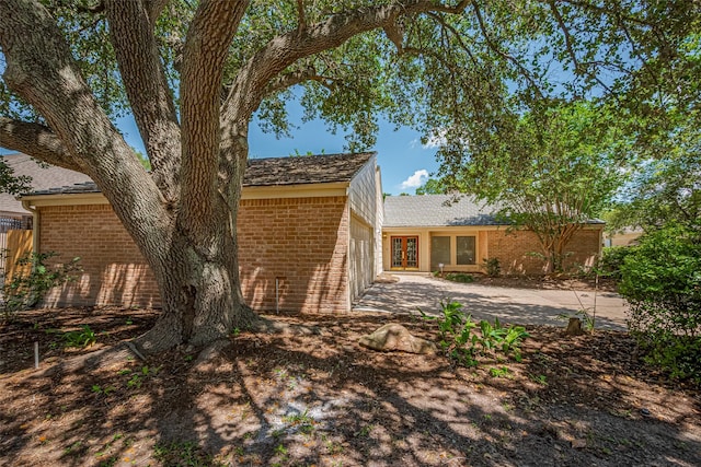 rear view of property featuring brick siding, a garage, french doors, driveway, and a patio area