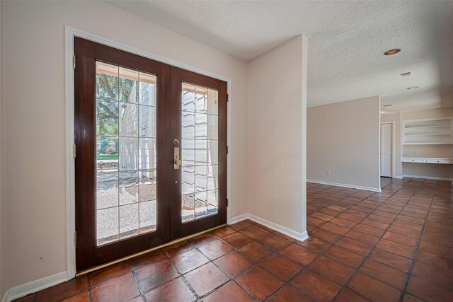 foyer with french doors, a textured ceiling, baseboards, and dark tile patterned floors