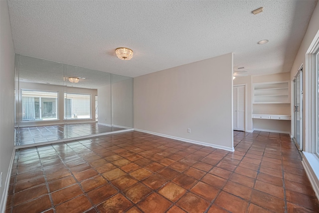 unfurnished room featuring a textured ceiling, tile patterned floors, baseboards, and built in features