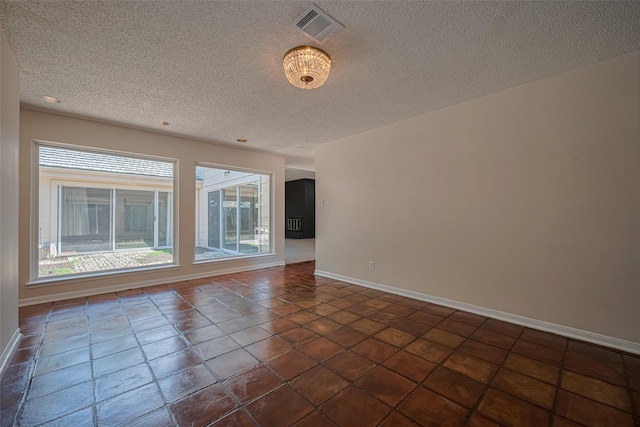 empty room featuring a textured ceiling, baseboards, and dark tile patterned floors