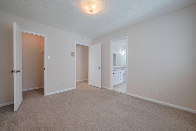 unfurnished bedroom with a spacious closet, light carpet, a textured ceiling, ensuite bath, and a closet
