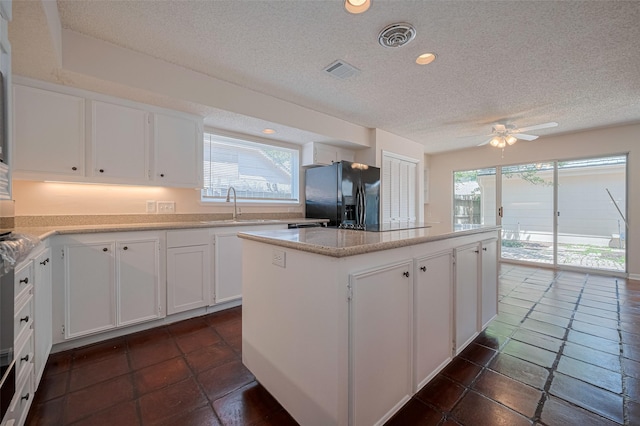 kitchen with black refrigerator with ice dispenser, a textured ceiling, a center island, healthy amount of natural light, and a sink