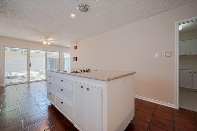 kitchen with a textured ceiling, ceiling fan, black electric stovetop, a kitchen island, and white cabinets