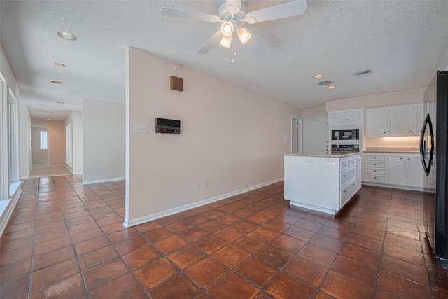 kitchen featuring black appliances, a textured ceiling, white cabinetry, a center island, and baseboards