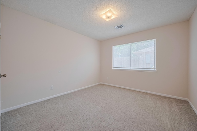 spare room with light colored carpet, a textured ceiling, and baseboards