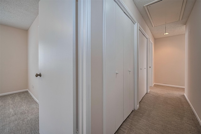 hallway with a textured ceiling, light carpet, attic access, and baseboards