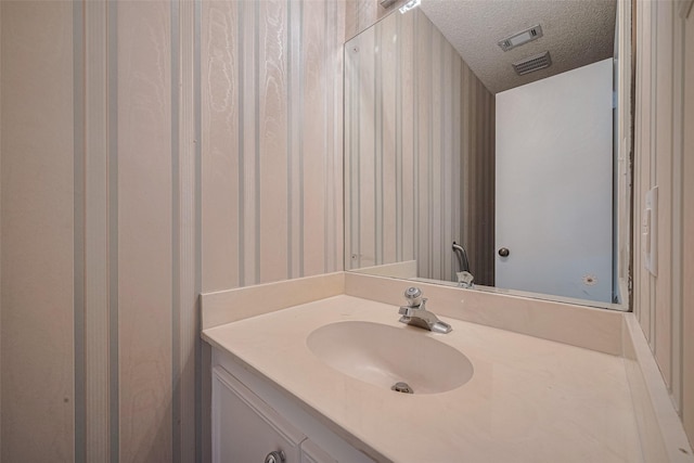 bathroom featuring a textured ceiling, vanity, and wallpapered walls