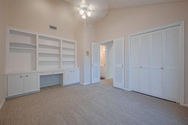 unfurnished bedroom featuring light colored carpet, a towering ceiling, baseboards, and ceiling fan