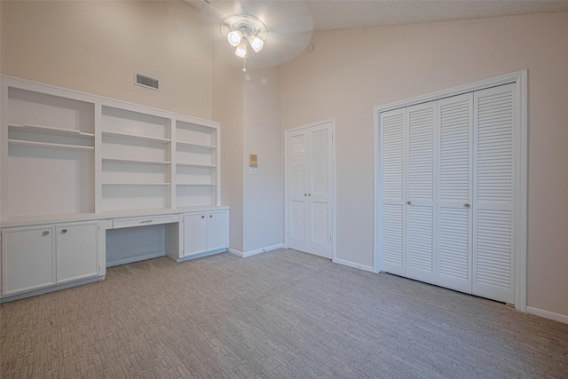 unfurnished bedroom featuring light colored carpet, a towering ceiling, two closets, baseboards, and ceiling fan