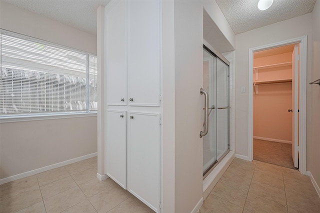 full bath featuring a stall shower, a textured ceiling, tile patterned floors, a spacious closet, and baseboards