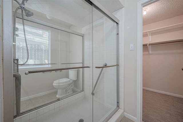 full bath featuring a shower stall, a textured ceiling, baseboards, toilet, and a walk in closet