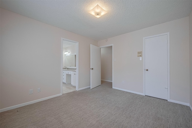 unfurnished bedroom with light colored carpet, a textured ceiling, connected bathroom, and baseboards