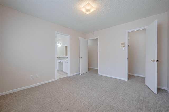 unfurnished bedroom featuring light carpet, a textured ceiling, connected bathroom, and baseboards
