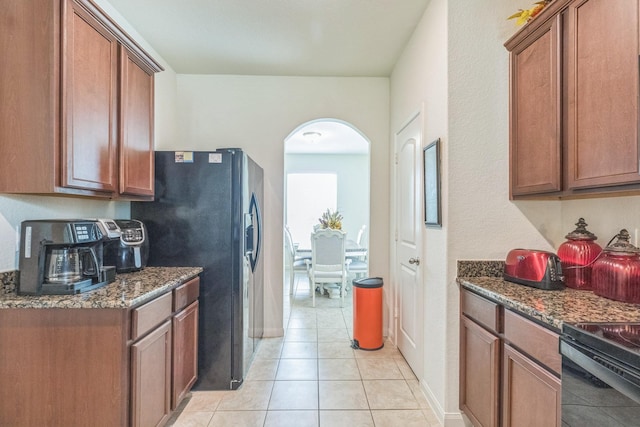 9526 Opal Gates Dr, Rosharon, TX 77583 - kitchen with arched walkways, dark stone countertops, brown cabinets, light tile patterned floors, and baseboards
