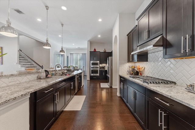10442 Lake Palmetto Dr, Conroe, TX 77385 - kitchen with under cabinet range hood, stainless steel appliances, backsplash, a sink, and hanging light fixtures
