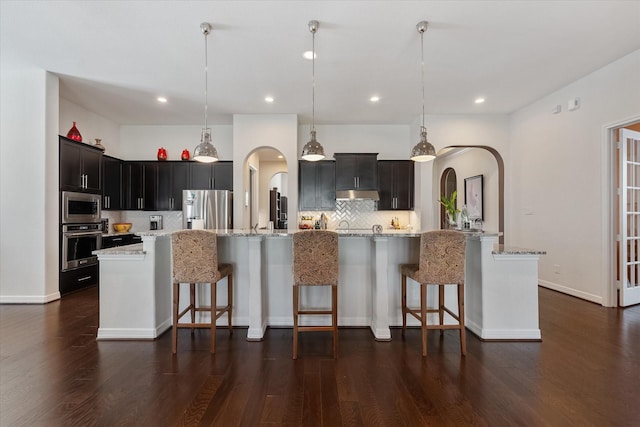 10442 Lake Palmetto Dr, Conroe, TX 77385 - kitchen featuring stainless steel appliances, arched walkways, backsplash, dark wood finished floors, and recessed lighting
