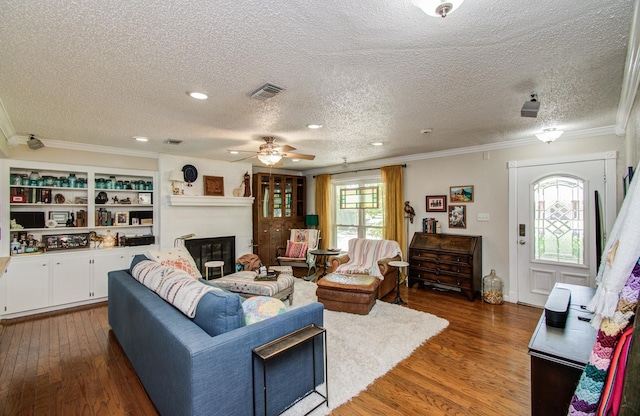 12211 3rd St, Santa Fe, TX 77510 - living area with wood finished floors, a textured ceiling, a ceiling fan, a glass covered fireplace, and crown molding