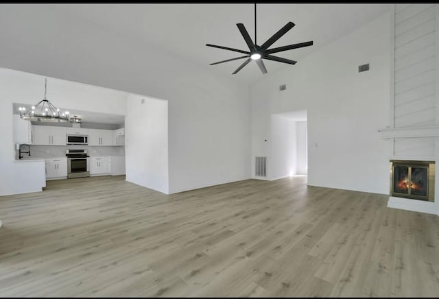 964 Lake View Dr, Montgomery, TX 77356 - unfurnished living room featuring high vaulted ceiling, ceiling fan, light wood-type flooring, a chandelier, and a large fireplace