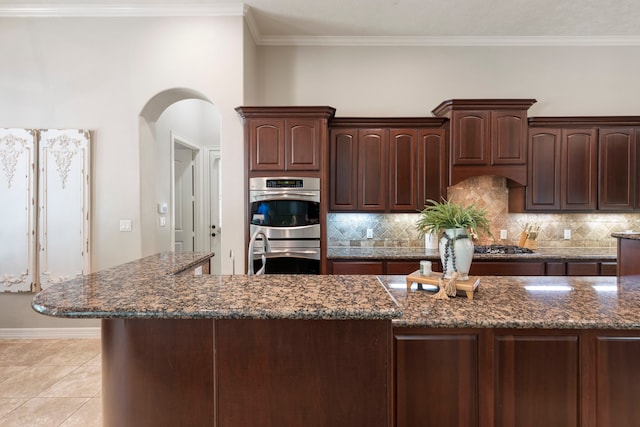 15557 Crown Oaks Dr, Montgomery, TX 77316 - kitchen with backsplash, double oven, arched walkways, dark stone counters, and dark brown cabinets