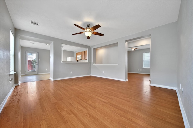 unfurnished living room featuring a ceiling fan, wood finished floors, plenty of natural light, and baseboards
