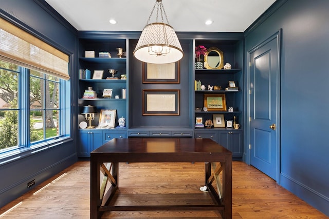 office space with healthy amount of natural light, built in shelves, light wood finished floors, and crown molding