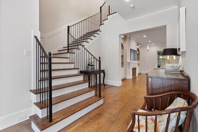 stairway with wood finished floors, recessed lighting, ornamental molding, and a fireplace