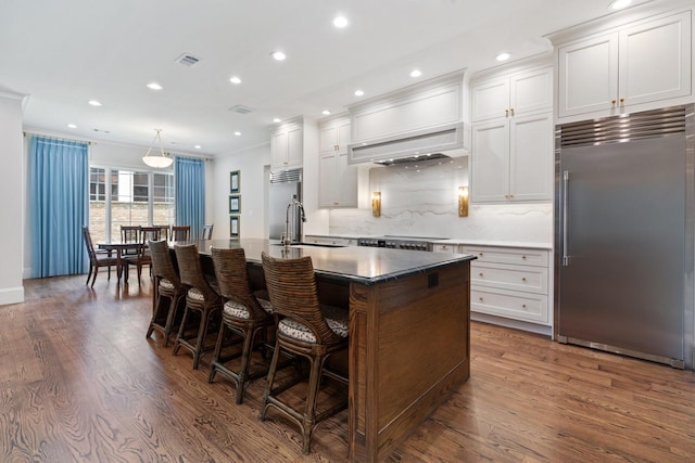 kitchen with stainless steel built in fridge, a sink, ornamental molding, an island with sink, and recessed lighting