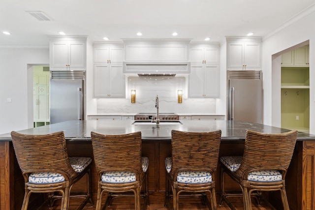 kitchen with stainless steel built in refrigerator, built in fridge, a large island, a sink, and white cabinetry