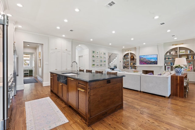 kitchen featuring arched walkways, crown molding, recessed lighting, light wood-type flooring, and a kitchen island with sink