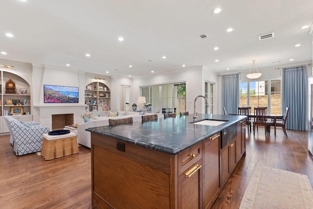 kitchen with a sink, wood finished floors, ornamental molding, brown cabinetry, and built in shelves