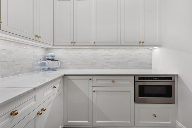kitchen featuring stainless steel oven, tasteful backsplash, and light stone countertops