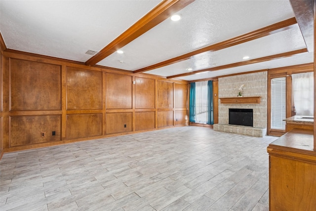 15623 Ensenada Dr, Houston, TX 77083 - unfurnished living room featuring beam ceiling, a decorative wall, light wood-type flooring, a brick fireplace, and a textured ceiling