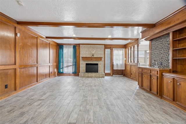 15623 Ensenada Dr, Houston, TX 77083 - unfurnished living room with a textured ceiling, light wood-style floors, beam ceiling, a sink, and a fireplace