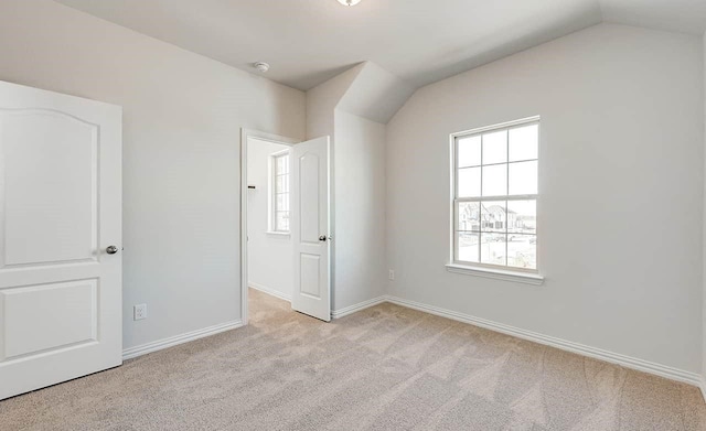 unfurnished bedroom featuring multiple windows, light colored carpet, lofted ceiling, and baseboards
