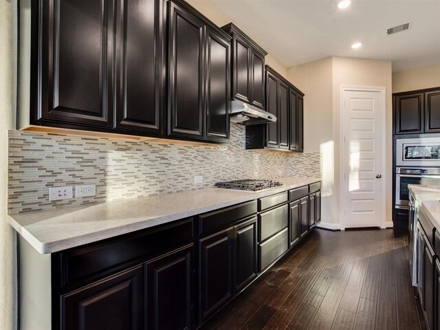 4218 Tanner Woods Ln, Sugar Land, TX 77479 - kitchen with stainless steel appliances, under cabinet range hood, baseboards, dark cabinets, and dark wood-type flooring