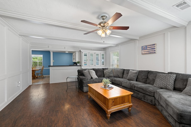 living area with beam ceiling, wood finished floors, a ceiling fan, crown molding, and a decorative wall