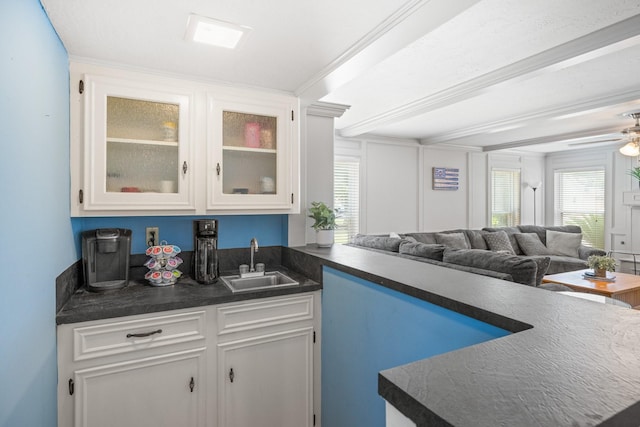 kitchen with a sink, dark countertops, open floor plan, glass insert cabinets, and white cabinets