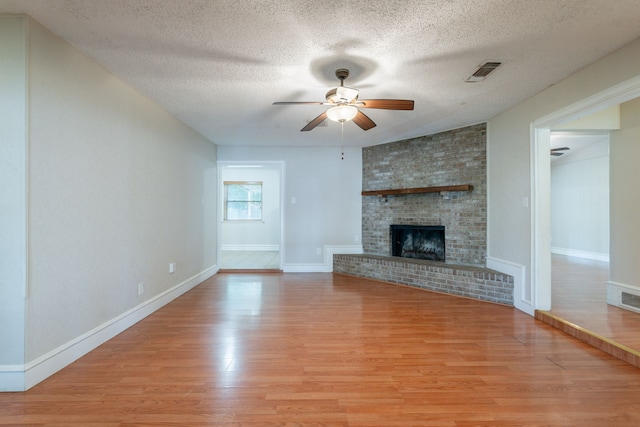 16466 Mandate Dr, Houston, TX 77049 - unfurnished living room featuring ceiling fan, light wood-type flooring, a textured ceiling, a fireplace, and baseboards