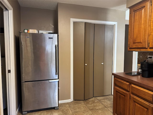 618 Hickory St, Huntsville, TX 77320 - kitchen with freestanding refrigerator, dark countertops, decorative backsplash, brown cabinets, and baseboards