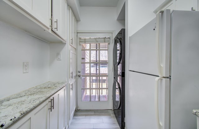 716 Bering Dr Unit 30, Houston, TX 77057 - kitchen featuring freestanding refrigerator, stacked washing machine and dryer, white cabinetry, and light stone counters