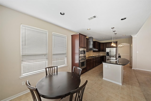 kitchen with stainless steel appliances, wall chimney range hood, dark countertops, a sink, and decorative backsplash