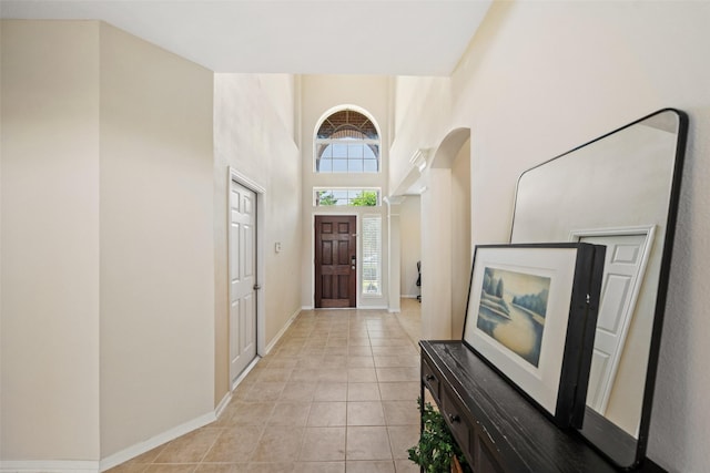 entryway with light tile patterned floors, a high ceiling, and baseboards