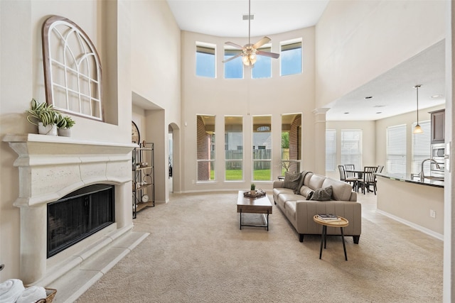 living area with ceiling fan, light carpet, a high ceiling, a fireplace, and baseboards