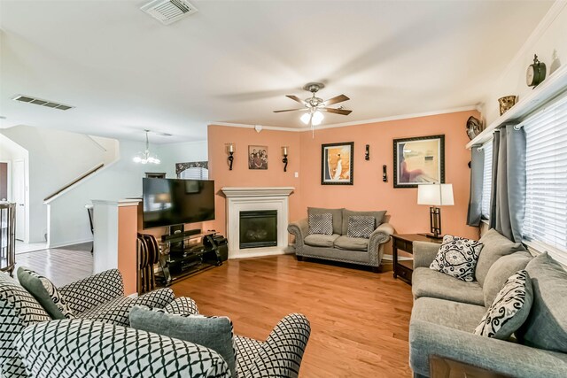 307 Squall Ct, Crosby, TX 77532 - living room featuring light wood-type flooring, ceiling fan, a chandelier, ornamental molding, and a fireplace with raised hearth
