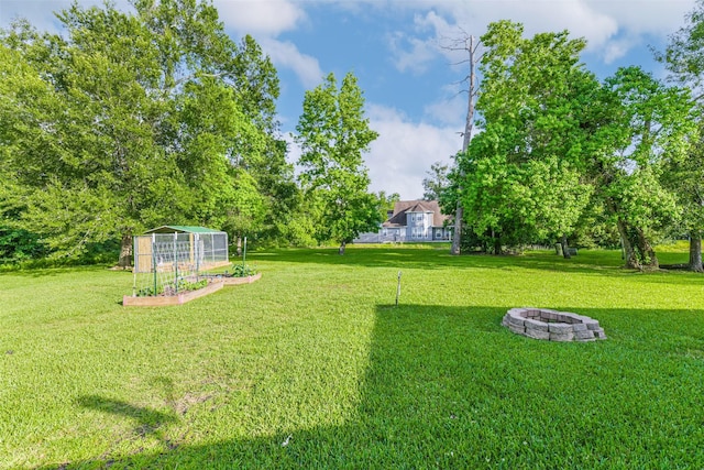 307 Squall Ct, Crosby, TX 77532 - view of green lawn with a fire pit, a vegetable garden, a greenhouse, and an outbuilding