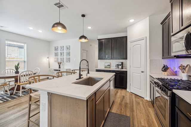 204 Catalina Cove Dr, Katy, TX 77493 - kitchen featuring appliances with stainless steel finishes, a sink, decorative backsplash, light wood-type flooring, and an island with sink