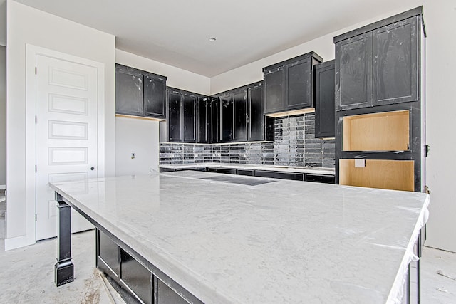 177 Peninsula Point Dr, Montgomery, TX 77356 - kitchen with dark cabinetry, backsplash, cooktop, light stone counters, and a kitchen island