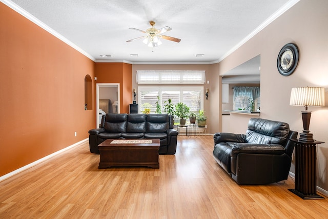 living room with light wood-style flooring, a ceiling fan, baseboards, crown molding, and arched walkways